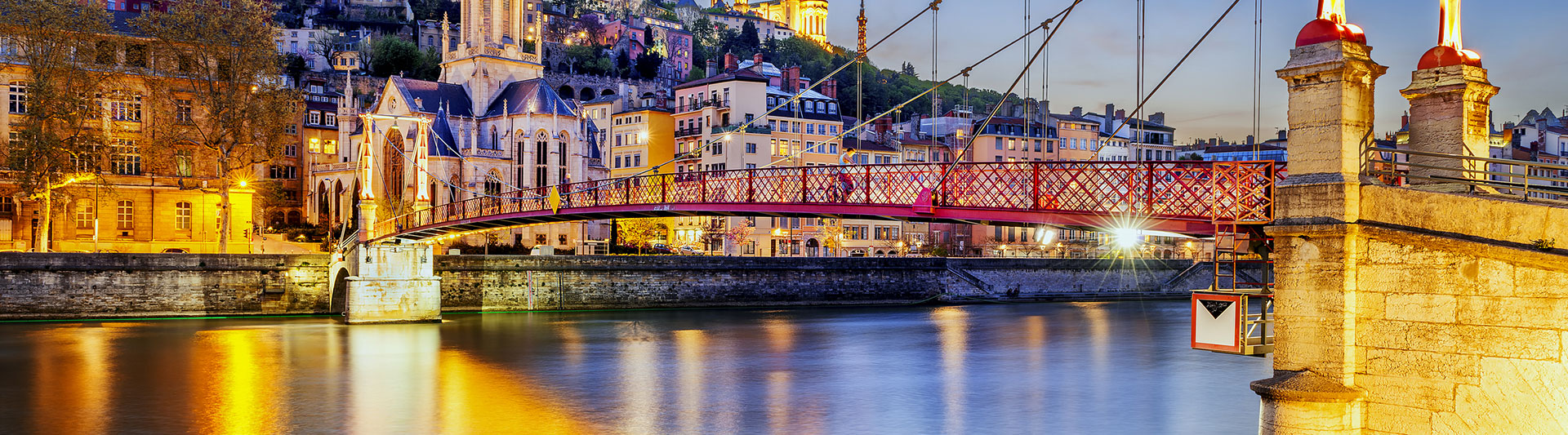 Red footbridge over the Saône in Lyon with the old town lit at dusk
